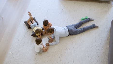 Top-view-of-sibling-kids-and-dad-sitting-and-lying-on-warm-floor