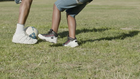 Legs-closeup-of-father-and-son-playing-football-in-summer-park.