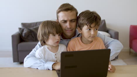 Serious-dad-working-on-laptop-and-embracing-sons