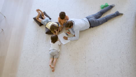 Top-view-of-sibling-children-and-dad-sitting-and-lying-on-floor