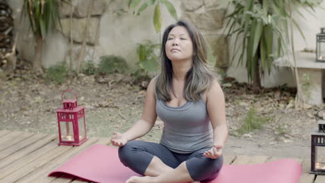 Long-shot-of-carefree-Japanese-woman-meditating-in-backyard