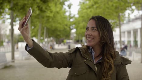Mujer-Joven-Sonriente-Tomando-Selfie-Con-Teléfono-Inteligente-Al-Aire-Libre.