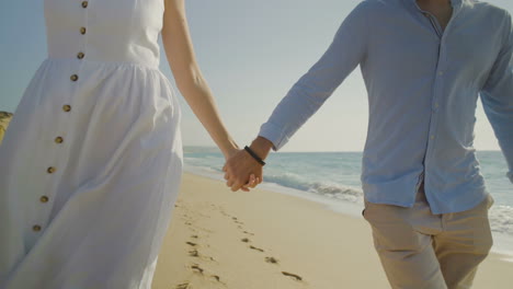 Mid-section-of-couple-holding-hands-on-sandy-beach