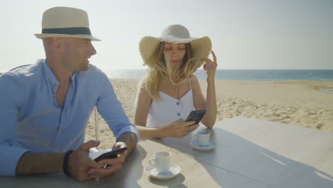 Young-couple-using-mobile-phones-on-beach