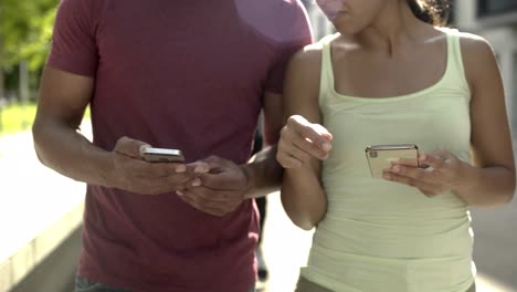 Cropped-shot-of-couple-holding-devices-while-walking-on-street