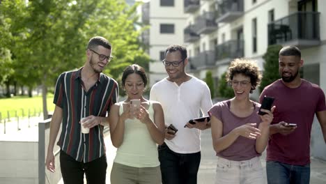 Happy-friends-with-smartphones-walking-on-street.