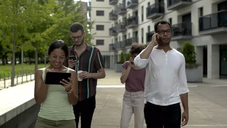 Smiling-young-people-with-digital-devices-strolling-on-street.