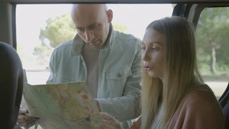 Focused-couple-discussing-map-at-car