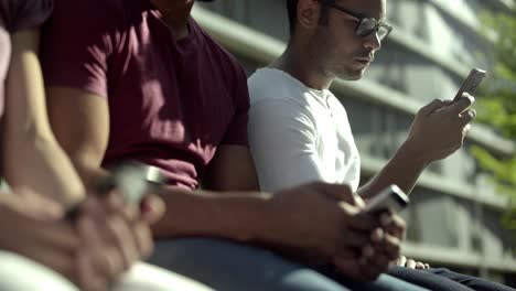 Focused-male-friends-sitting-in-park-and-using-smartphones.