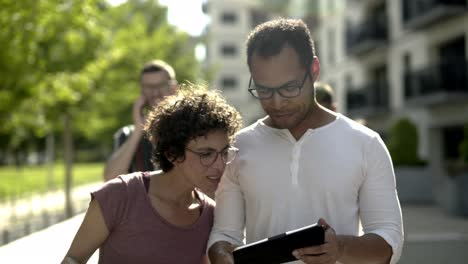 Smiling-couple-in-eyeglasses-holding-devices-on-street