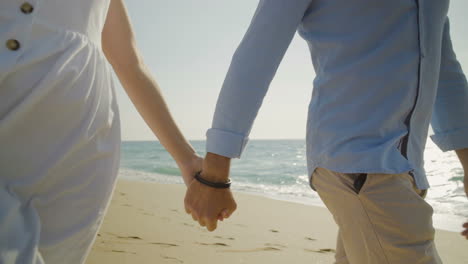 Cropped-shot-of-couple-holding-hands-and-walking-on-beach