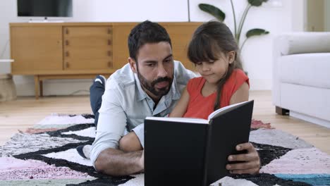Little-girl-and-her-dad-relaxing-on-floor-and-reading-book