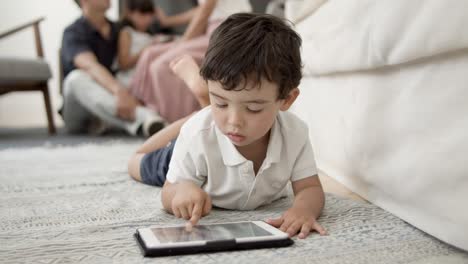 Sweet-little-boy-with-tablet-lying-on-floor-in-living-room