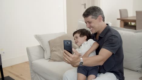 Papá-Feliz-Y-Pequeño-Hijo-Activo-Usando-Un-Teléfono-Inteligente-Juntos