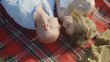 Top-view-of-couple-lying-on-plaid-at-beach