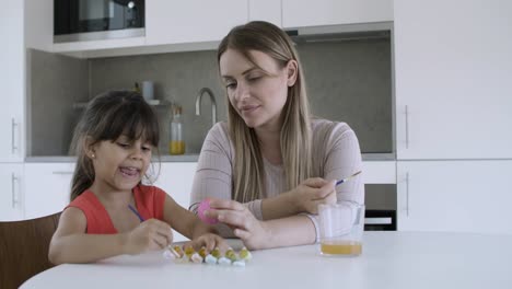 Mom-helping-little-girl-to-paint-egg-at-dining-table