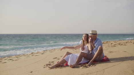 Couple-sitting-on-plaid-at-sandy-beach