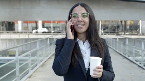Cheerful-businesswoman-talking-by-smartphone-on-street