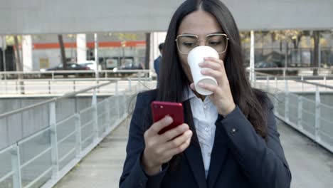 Businesswoman-with-coffee-to-go-using-smartphone-on-street