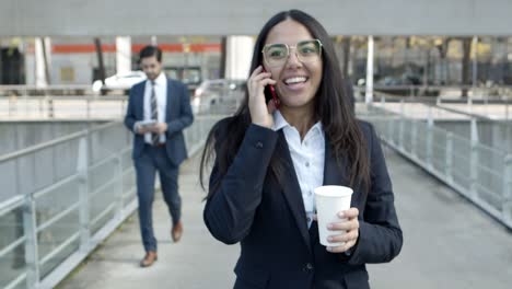 Smiling-businesswoman-talking-by-cell-phone-on-street