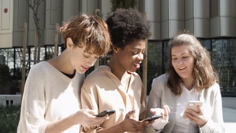 Three-women-with-smartphones-sitting-on-street