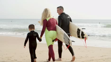 Familia-Feliz-De-Surfistas-Caminando-Por-La-Costa