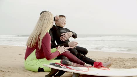 Cheerful-family-in-wetsuits-sitting-in-beach