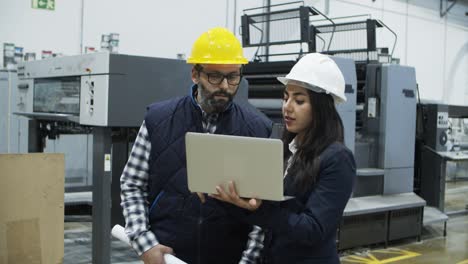 Focused-factory-workers-talking-while-standing-with-laptop