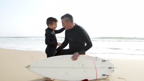 Father-and-son-in-wetsuits-talking-on-beach
