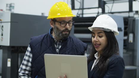 Focused-factory-employees-talking-while-standing-with-laptop