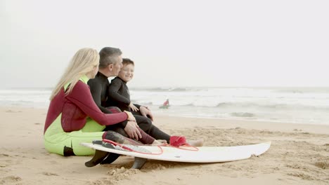 Happy-family-in-wetsuits-sitting-in-beach