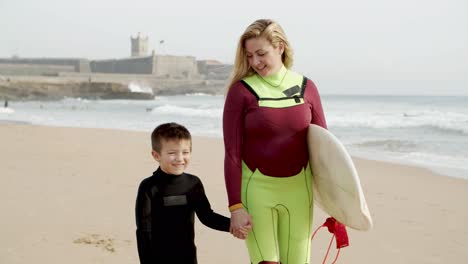Surfista-Femenina-Con-Un-Hijo-Pequeño-Caminando-Por-La-Playa