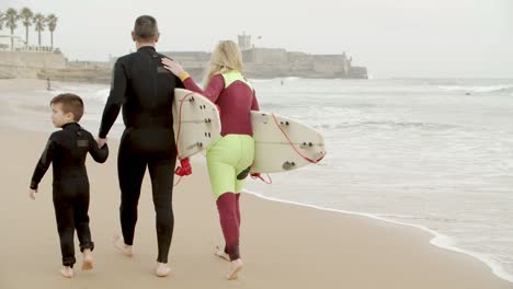 Family-with-surfboards-walking-on-beach