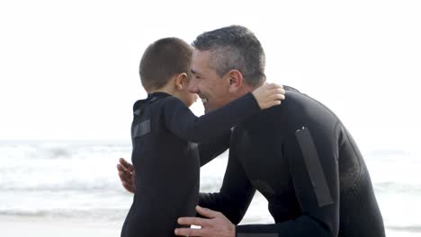 Father-and-son-in-wetsuits-hugging-on-beach