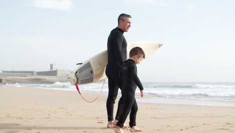 Father-and-son-in-wetsuits-walking-on-beach