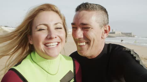 Happy-couple-in-wetsuits-smiling-at-camera