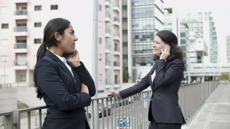 Businesswomen-talking-by-smartphones-on-street