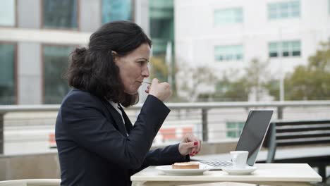 Mujer-De-Negocios-Usando-Laptop-Y-Comiendo-Postre-En-La-Cafetería