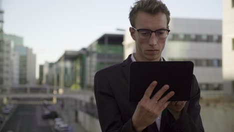Good-looking-man-standing-outside,-working-on-tablet
