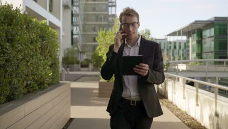 Man-walking-outside,-talking-on-phone,-looking-at-tablet