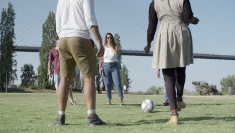 Group-of-five-happy-friends-kicking-ball-in-park.