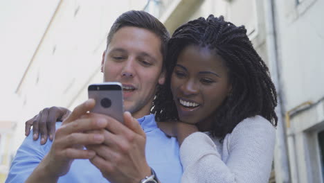 Smiling-multiracial-couple-with-smartphone-outdoor.