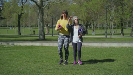 Front-view-of-women-in-park-holding-yoga-mat-in-hands,-talking