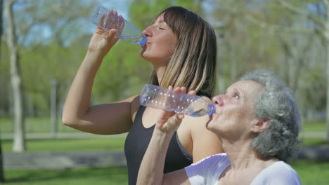 Young-and-middle-aged-women-in-park-drinking-water-after-jogging