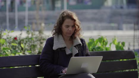 Focused-middle-aged-woman-using-laptop-outdoor
