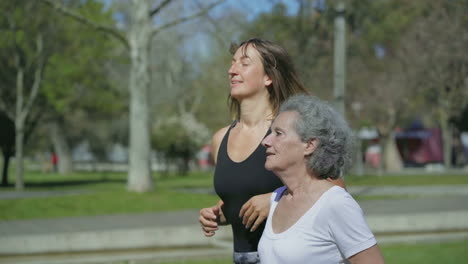 Side-view-of-two-women-jogging-in-park,-talking-and-smiling