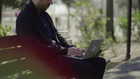 Concentrated-man-sitting-on-bench-and-working-with-laptop