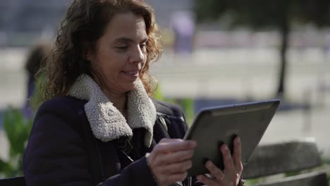 Mujer-Madura-Feliz-Vistiendo-Chaqueta-Con-Tablet-Al-Aire-Libre