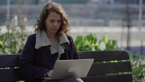 Thoughtful-mature-woman-typing-on-keyboard-of-laptop-outdoor
