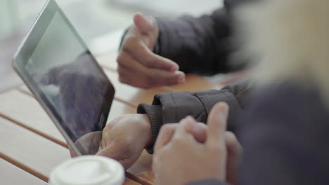Close-up-shot-of-Afro-American-middle-aged-mans-and-young-womans-hands-looking-for-data-on-tablet